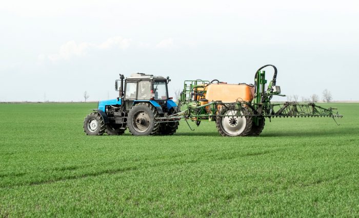 Tractor with high wheels is making fertilizer on young wheat. The use of finely dispersed spray chemicals. Tractor with a spray device for finely dispersed fertilizer.